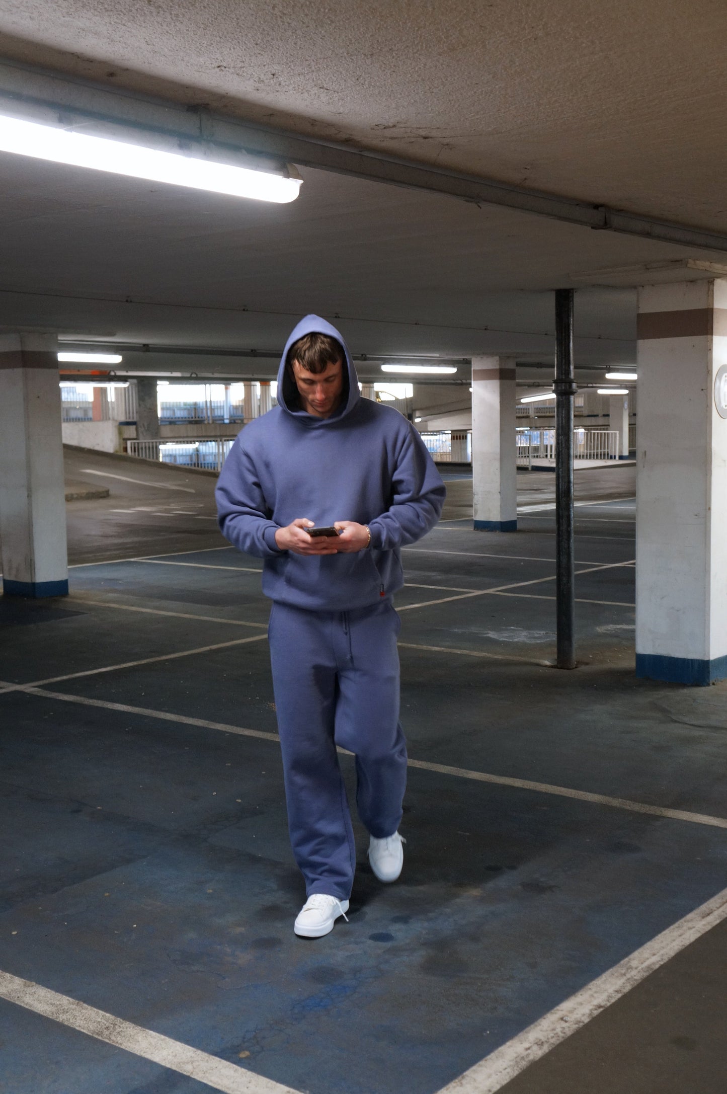 Person wearing a blue sos tracksuit standing in an underground parking lot.