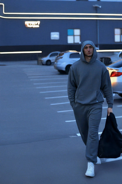 Man in gray sos hoodie and pants walking in a parking lot with cars in the background