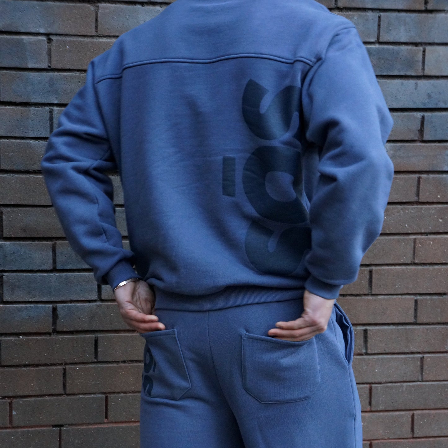 Person wearing a blue jumpsuit with a sos logo on the back against a brick wall.