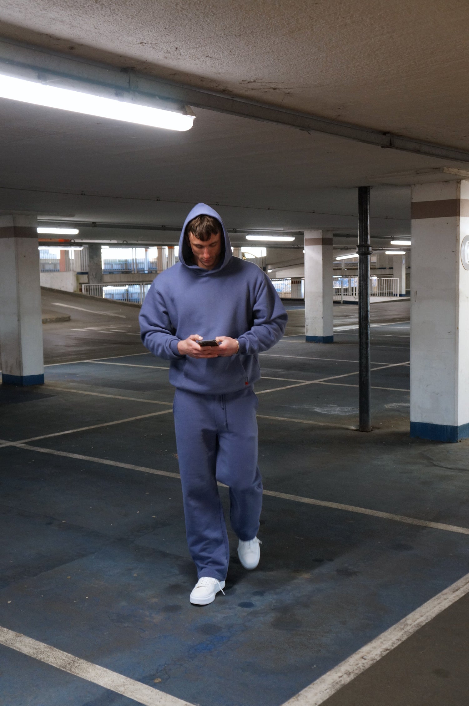 Person wearing a blue sos tracksuit standing in an underground parking lot.